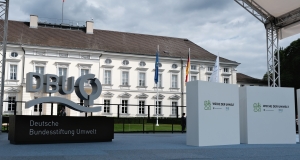 Das Logo der Deutschen Bundesstiftung Umwelt steht auf der Bühne der Woche der Umwelt. Im Hintergrund ist das Schloss Bellevue zu sehen.